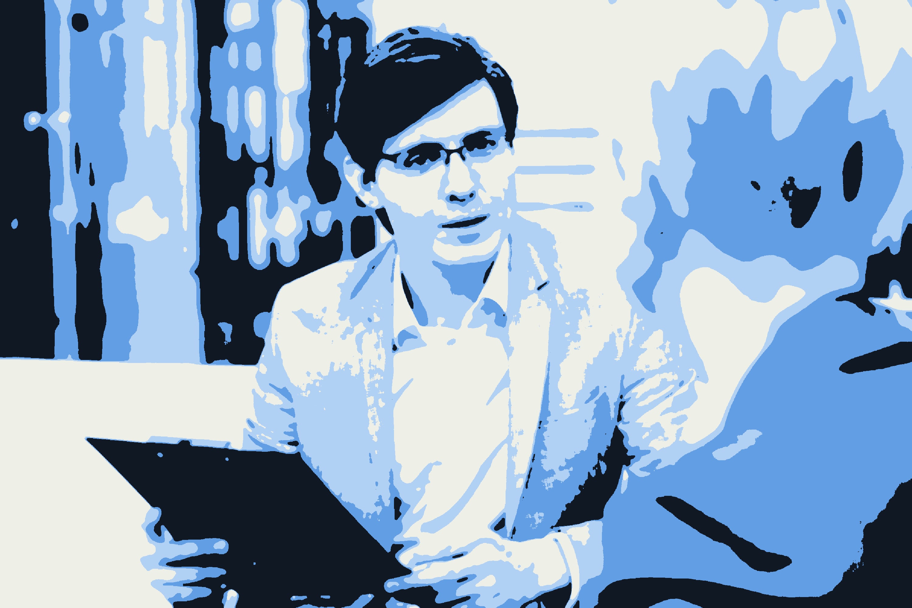 A man in glasses holding a clipboard, speaking with a colleague across a table.